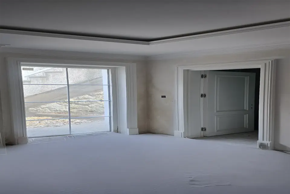 Geniş beyaz pervazlı pencere ve panelli çift kanatlı kapının bulunduğu oda
