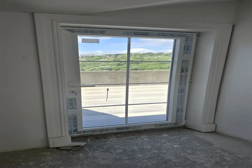 Tadilat sürerken balkon kapısını çevreleyen beyaz profilli ahşap pervaz