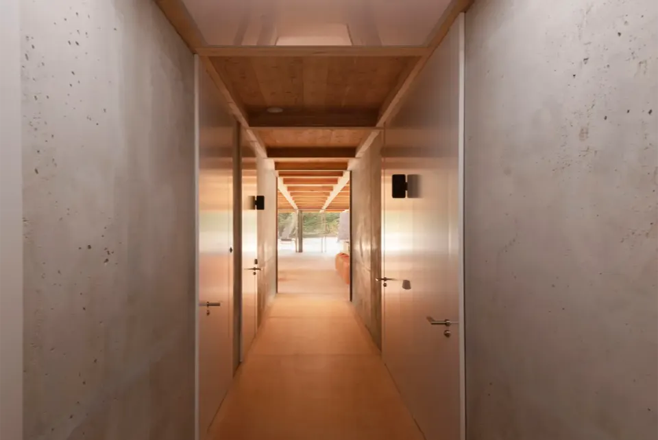 Brüt beton duvarlı koridorda beyaz kapılar ve ahşap tavanın ucundaki aydınlık salon